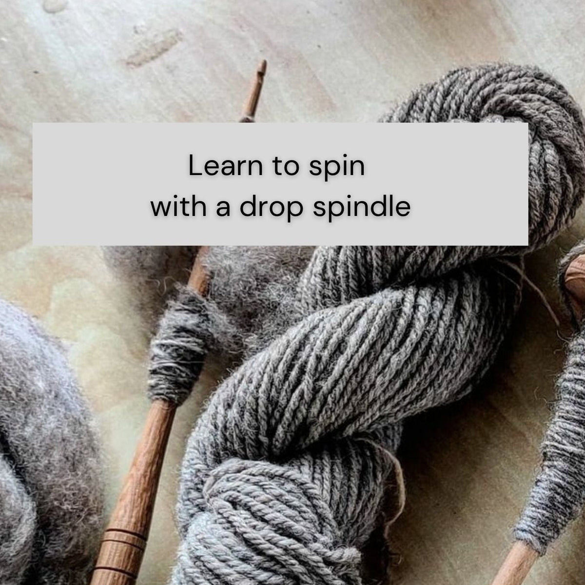 A styled flat-lay of gray yarn wrapped around wooden spinning needles, with text overlays reading 'Learn to spin with a drop spindle' and 'The Woven Briar www.TheWovenbriar.