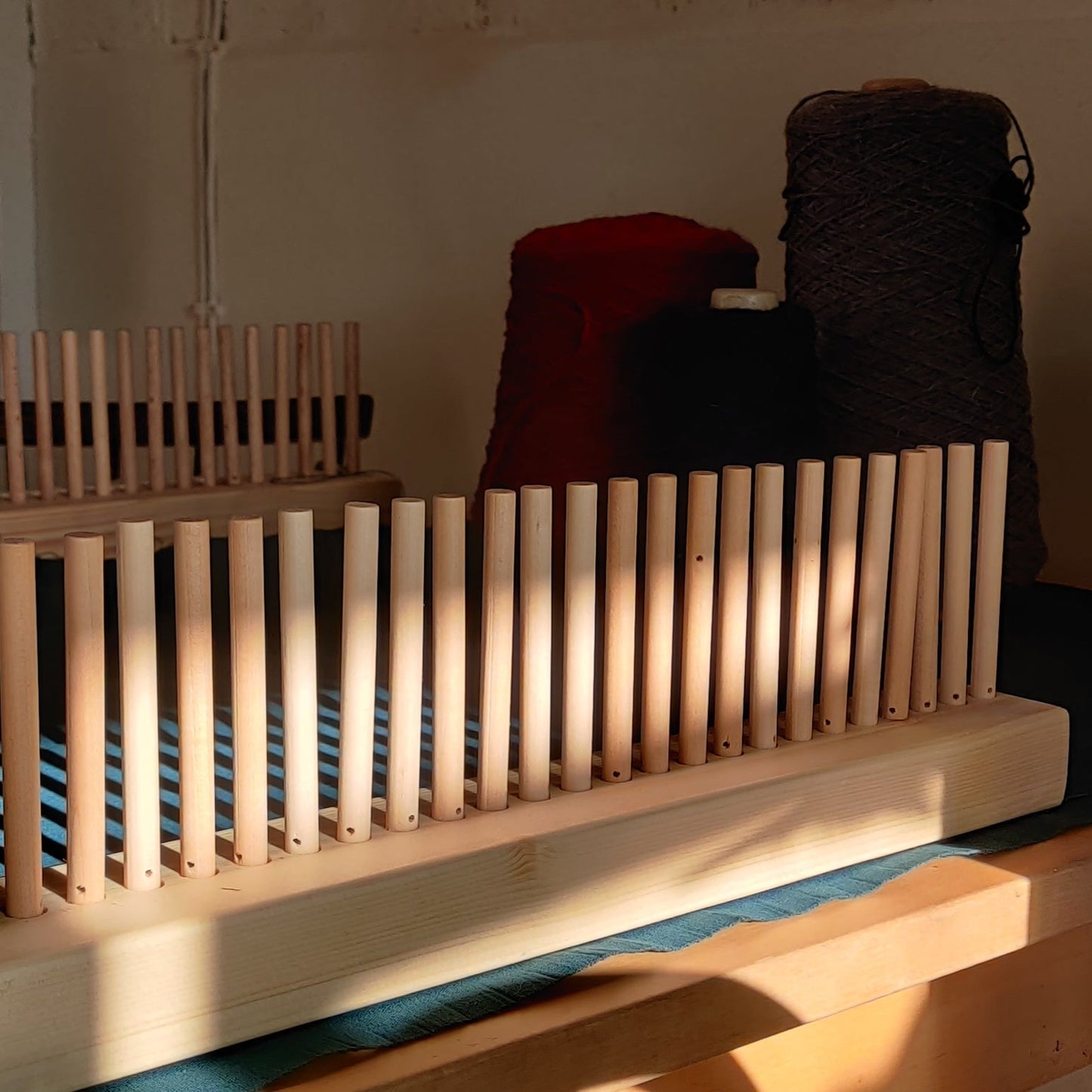 Image of a peg loom set with yarn in the background.