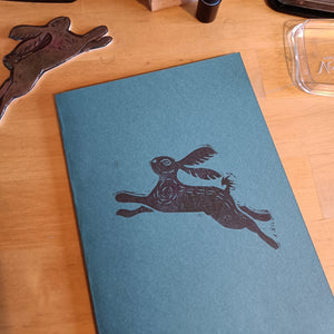 A blue notebook with a hand printed hare ont he cover in black