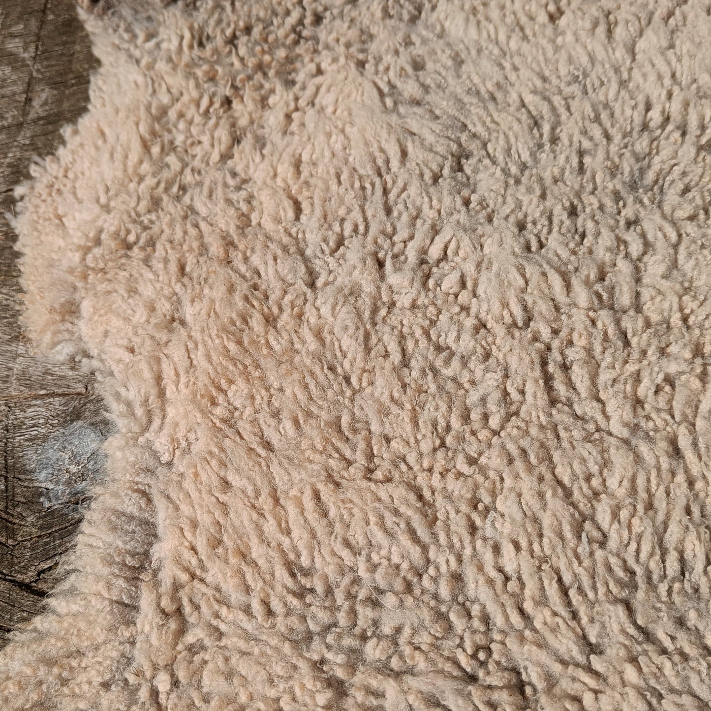 A close-up of a fluffy, shaggy beige rug or textile laid over a rustic weathered wood surface.