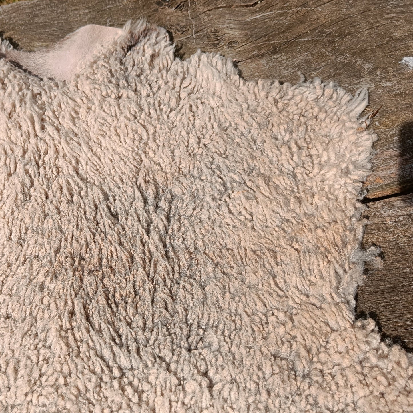 A close-up of a fluffy, shaggy sheepskin or faux-sheepskin rug in a light cream or off-white color, laid out on a weathered wooden surface.
