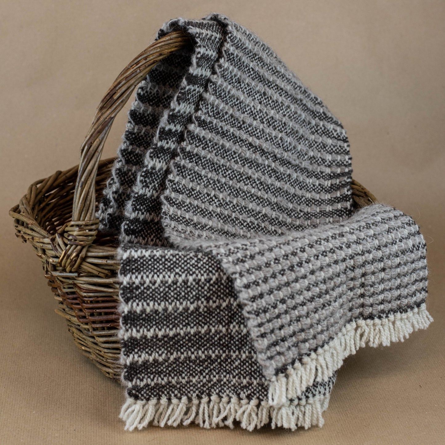 Woven blanket with black and white pattern draped over a wicker basket on a brown background