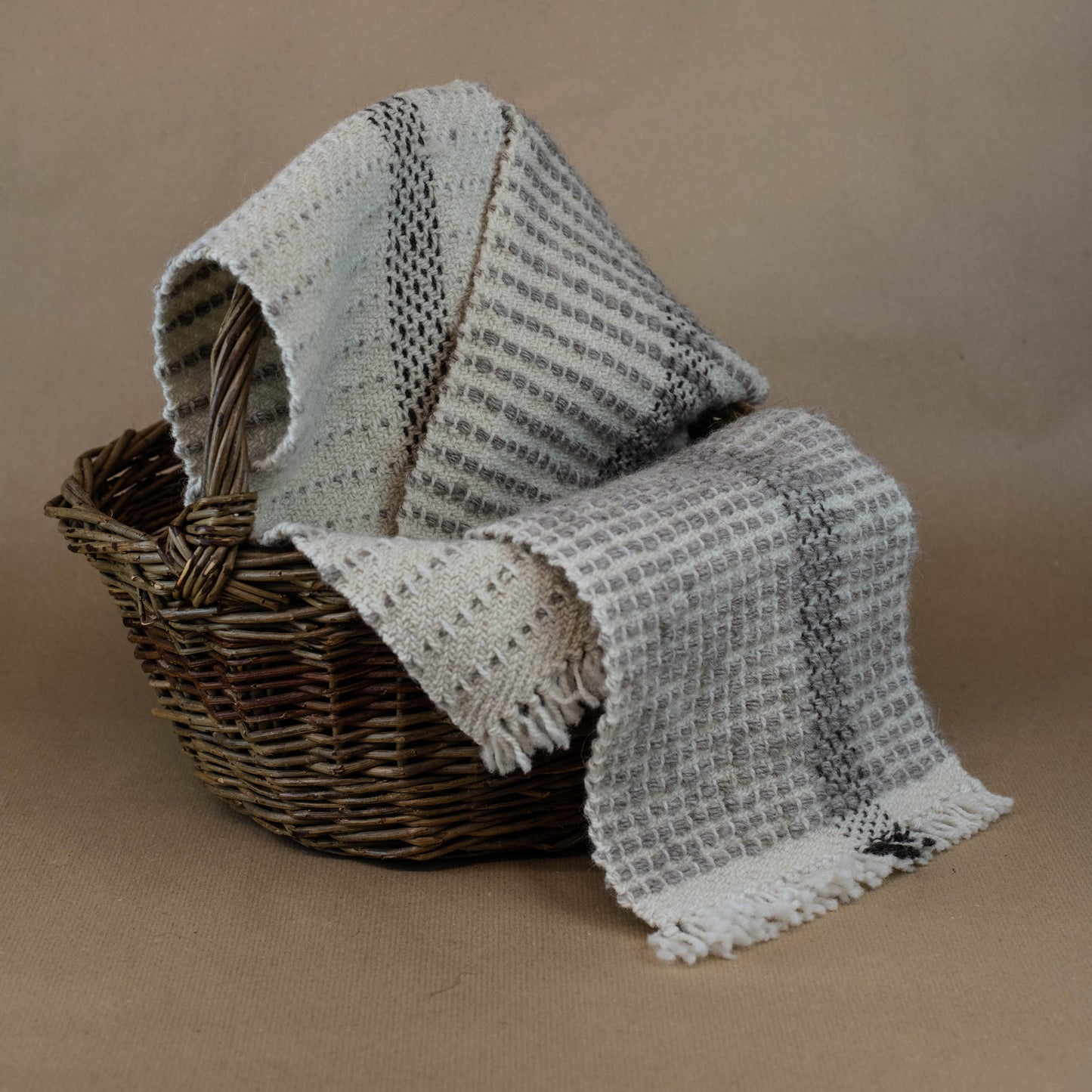 Textured blanket draped over a wicker basket on a brown background