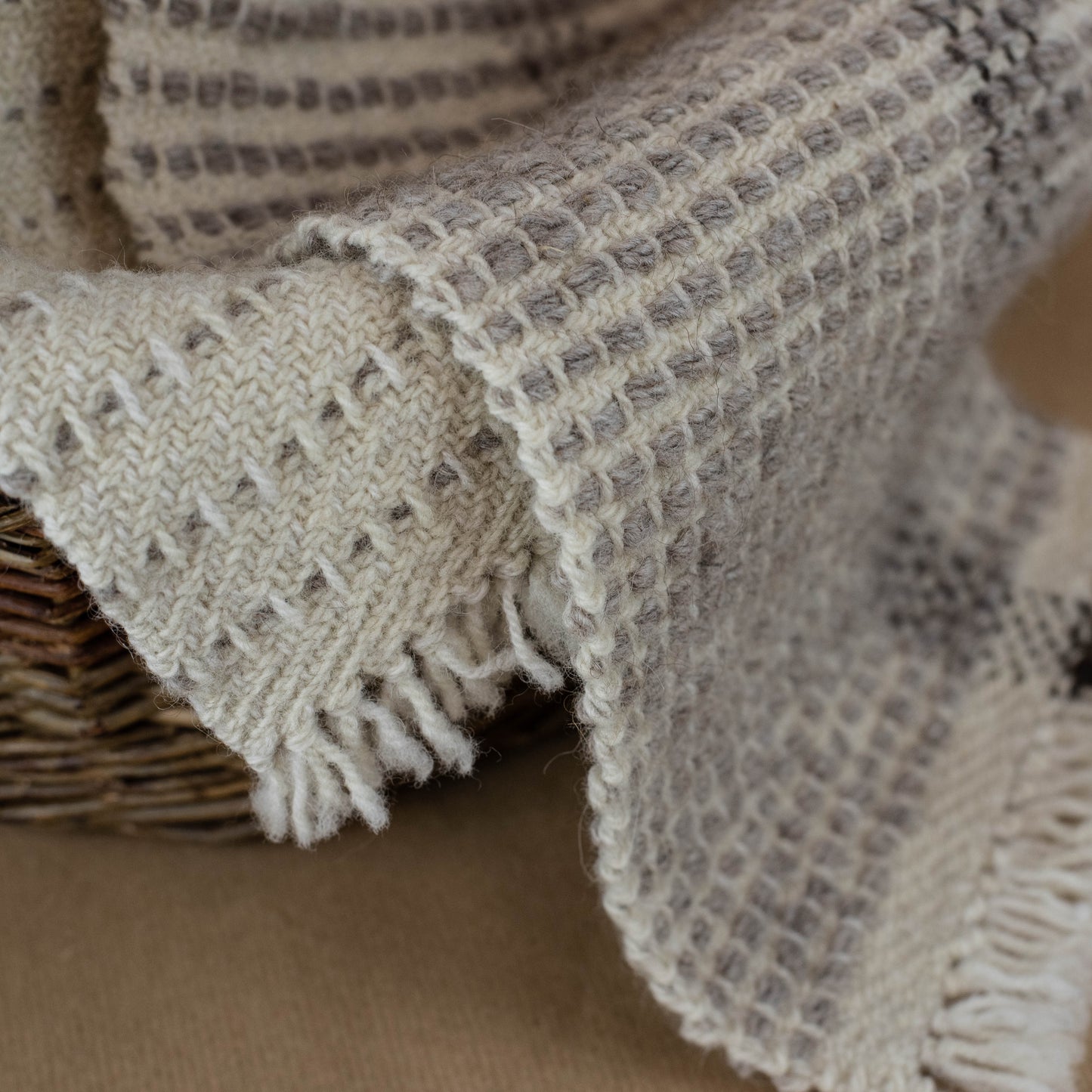 Textured blanket draped over a woven basket on a brown background