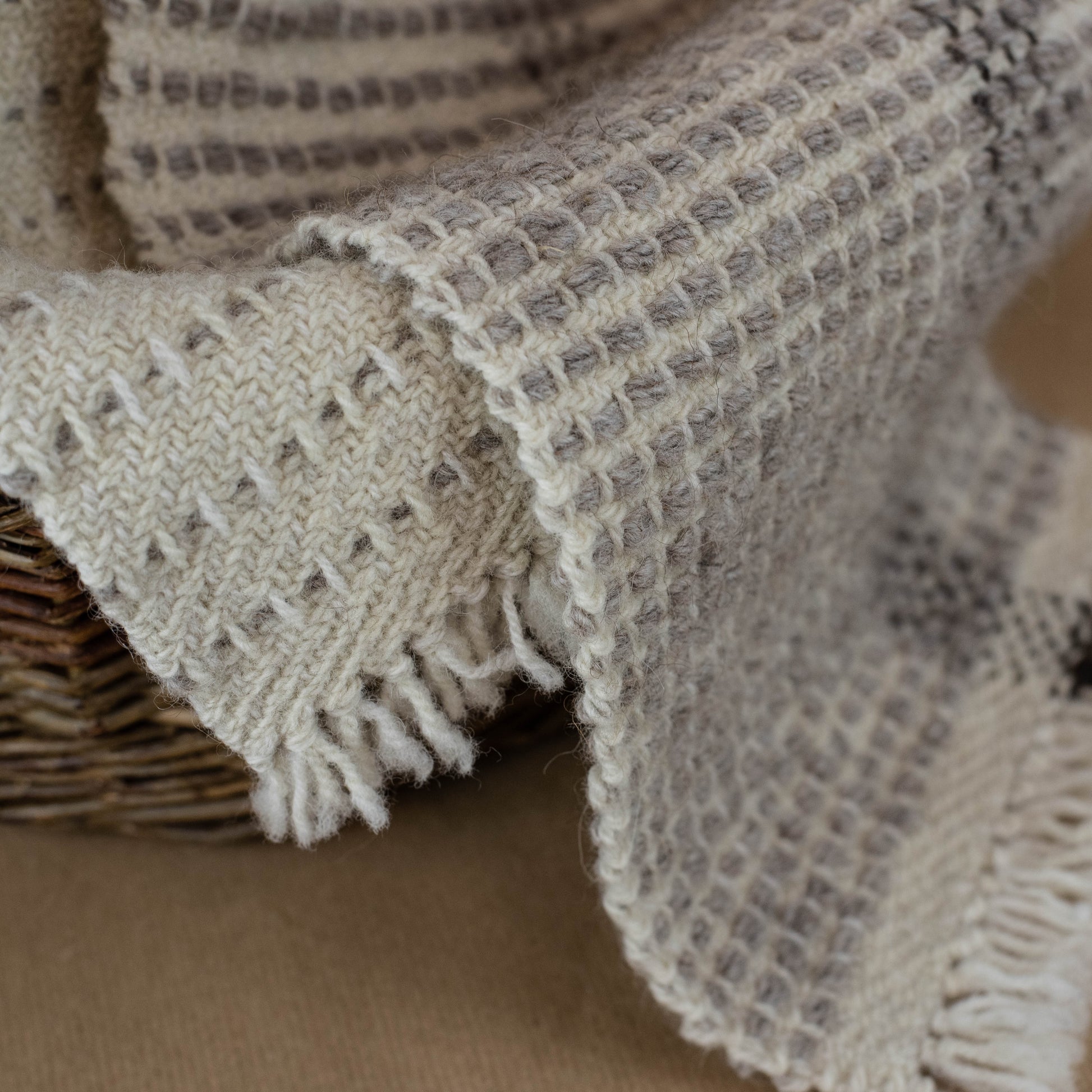 Textured blanket draped over a woven basket on a brown background