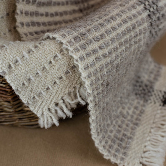 Textured blanket draped over a woven basket on a brown background