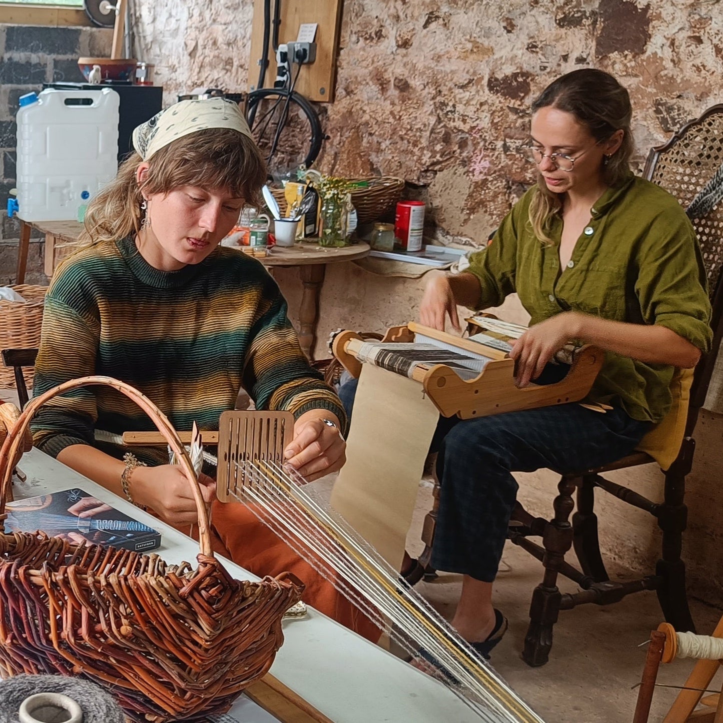 Two women people working with weaving equipment and a basket in a workshop setting.