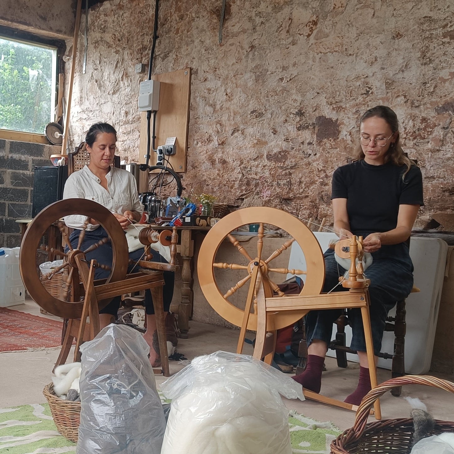 People sitting around a table with spinning wheels in a rustic room.