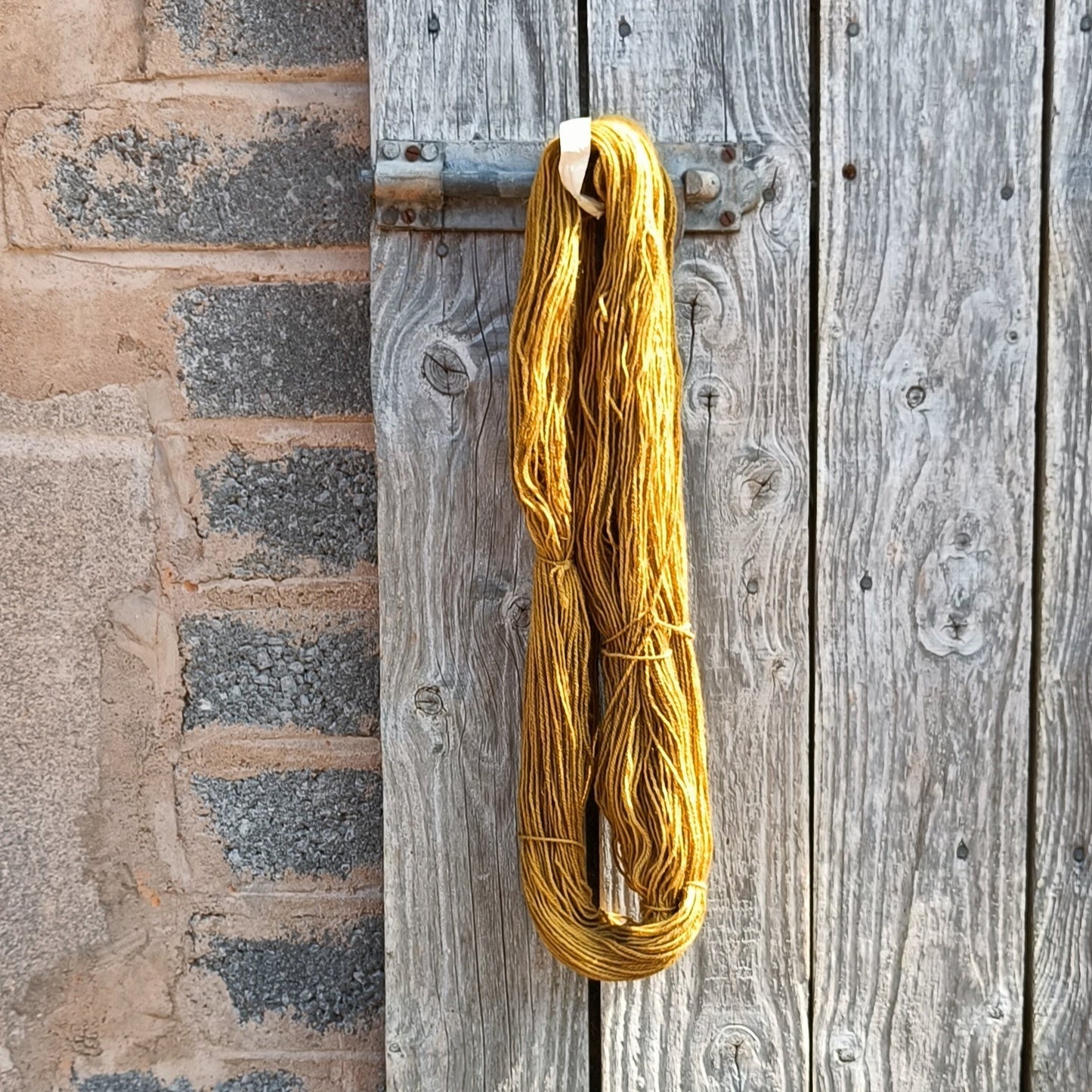 Yellow walnut-dyed yarn on a wooden hook against a brick wall
