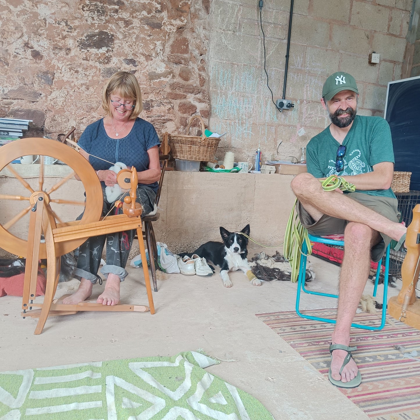 Two people sitting in a room with a spinning wheel and a dog.