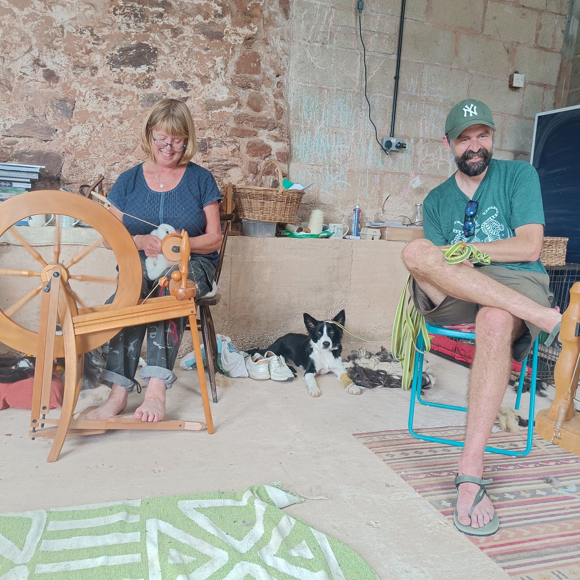 Two people sitting in a room with a spinning wheel and a dog.