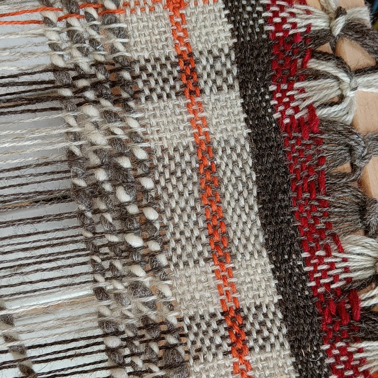 Woven fabric on a loom with visible threads and wooden frame.