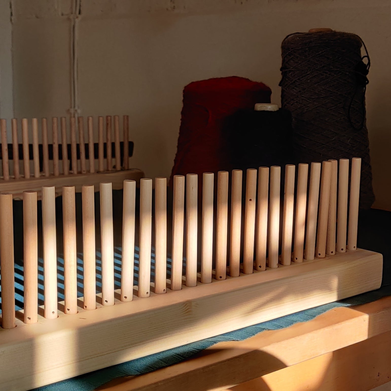 Image of a peg loom set with yarn in the background.