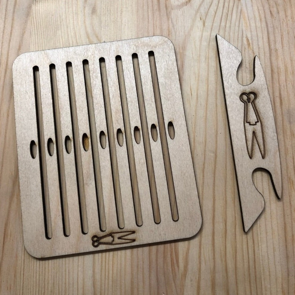 Photo shows a small wooden heddle and matching shuttle, both have the logo of The Woven Briar on them, which is an outline of a paid of blade shears.