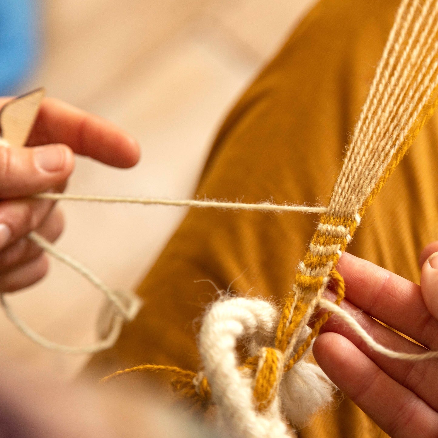 Two white skinned hands demonstrate weaving the white weft through the orange and white warp threads.